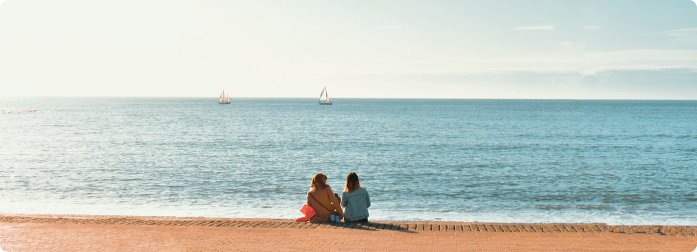 A family sitting together on a beach watching sailboats