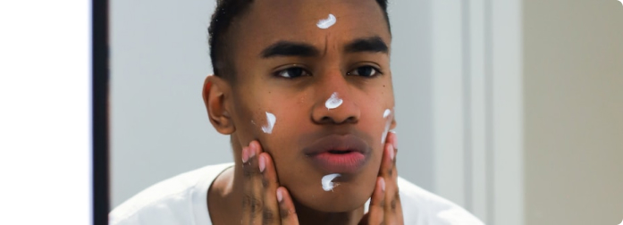 A man looking into a mirror and applying some face lotion