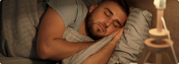 A male sleeping in bed with a bedside lamp still on