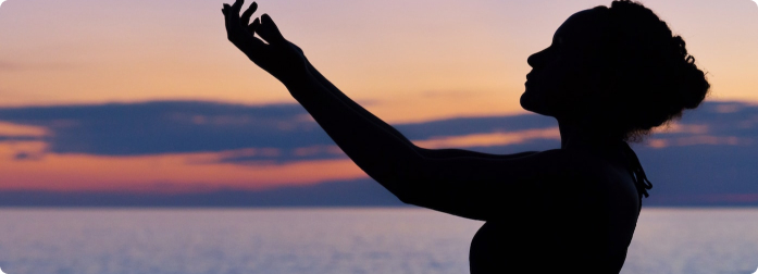 The silhouette of a woman with arms raised at sunrise