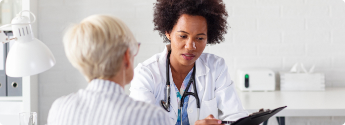 A doctor in medical coat, holding a chart, talking with a patient